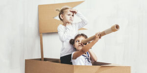 Two children little girls home in a cardboard ship play captains and sailors