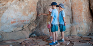 Two young boys and their sister pointing looking at traditional Busman paintings in a cave