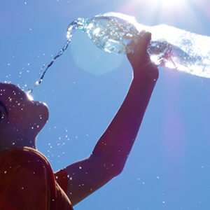 Child pouring water on himself. in silhouette with blue sky background.