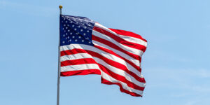 American flag waving on pole with bright vibrant red white and blue colors against blue sky