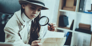 Child holding a magnifying glass looking at a paper clue