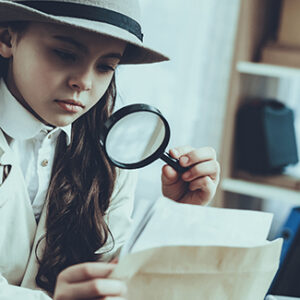 Child holding a magnifying glass looking at a paper clue