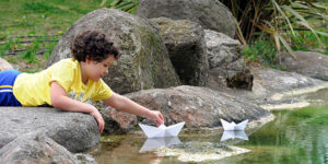 Child playing with a paper boat in a small stream of water
