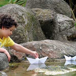 Child playing with a paper boat in a small stream of water