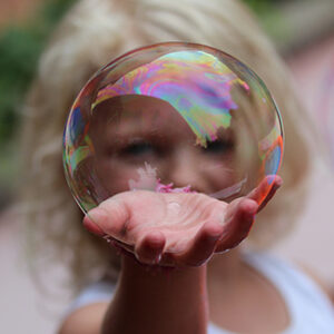 Girl with a soap bubble in her hand holding it up to the camera