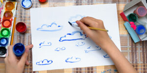 a girl drawing watercolor blue clouds on a blank white paper, artistic creation at home, makes creative artwork