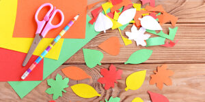 Colored paper sheets, scissors, pencil, autumn colored paper leaves on wooden background. Cutting with scissors. Development of skill for a toddler or preschooler. Top view